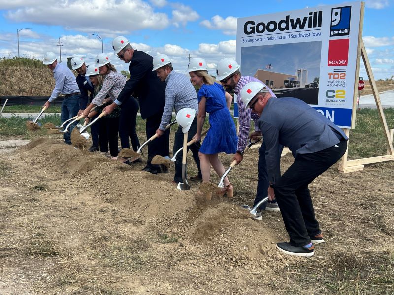 People in hard hats scooping earth at a groundbreaking.