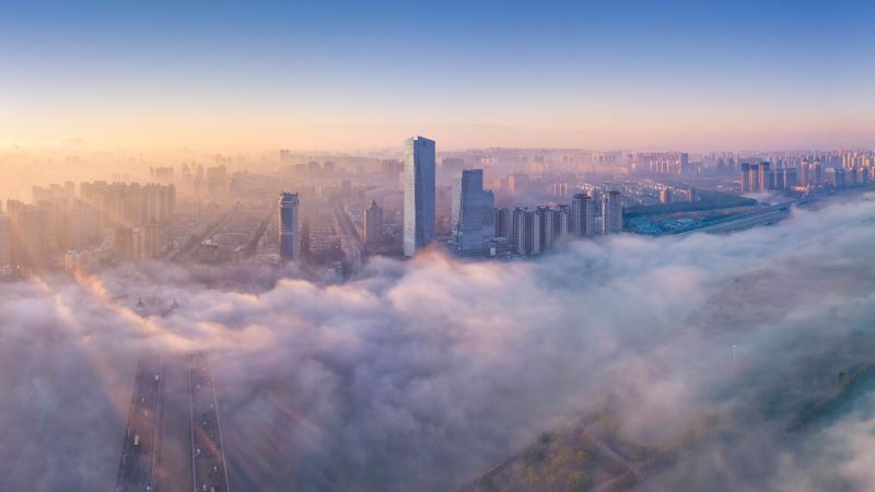 A bird's eye view of a city at sunrise with clouds in the foreground. 