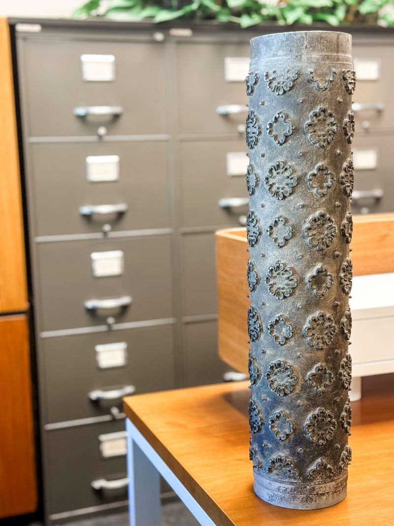 A vintage wallpaper roller sitting on an office desk. A metal filing cabinet is in the background. 