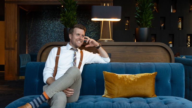 An architect sitting on a blue couch, looking in the distance and smiling. 